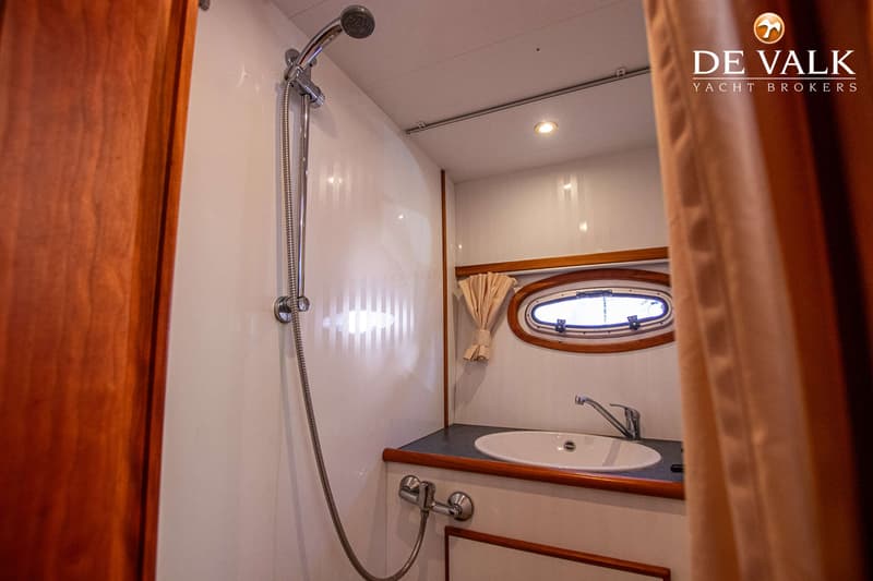 Een badkamer op een boot met een douche, wastafel, kraan en een ovaal patrijspoort. — Babro Newline 1290