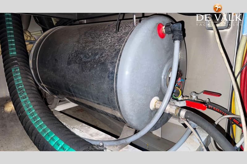 Een close-up van een boiler met diverse slangen en bedrading, gemonteerd op een metalen frame.