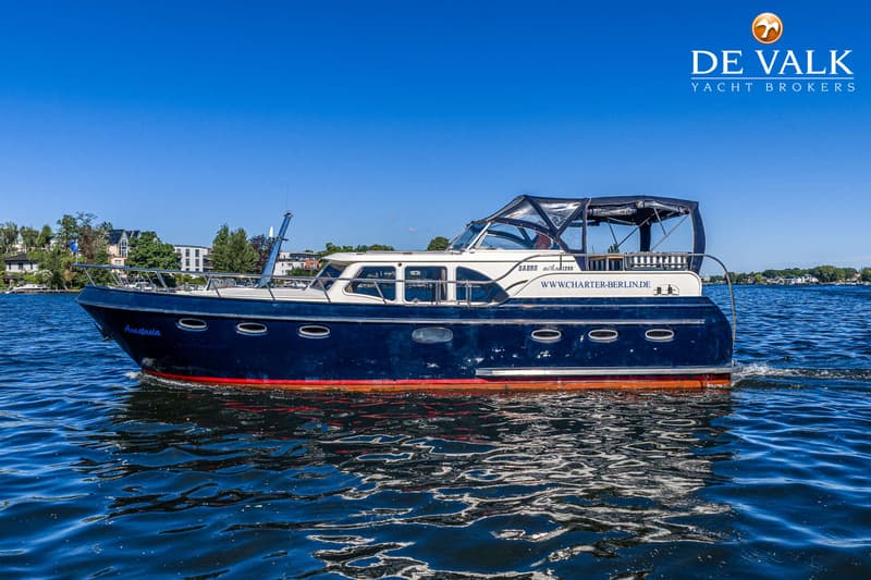 Een blauw-witte motorboot met de naam "Anastasia" vaart op een zonnige dag over water, met bebouwing op de achtergrond.