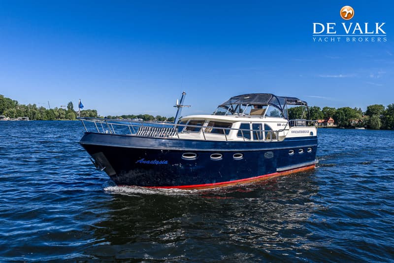 Een donkerblauwe motorboot met de naam "Anastasia" vaart op een waterweg onder een helderblauwe hemel. — Babro Newline 1290