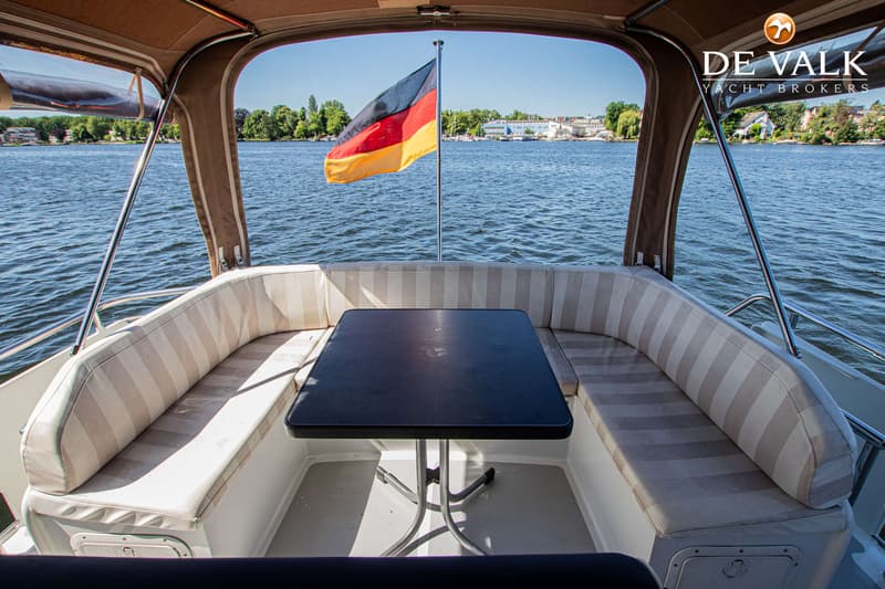 Een bootinterieur met een zwarte tafel, beige gestreepte banken en een Duitse vlag aan de achterkant, met water en…