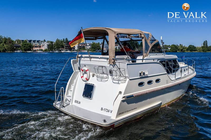 Een witte motorboot met een bruine kap vaart op blauw water, met een Duitse vlag aan de achtersteven. — Gruno 37 Classic