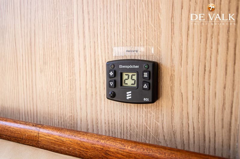 Een zwarte Eberspächer verwarmingsregelaar met een digitaal display dat '25' toont, gemonteerd op een houten wand.