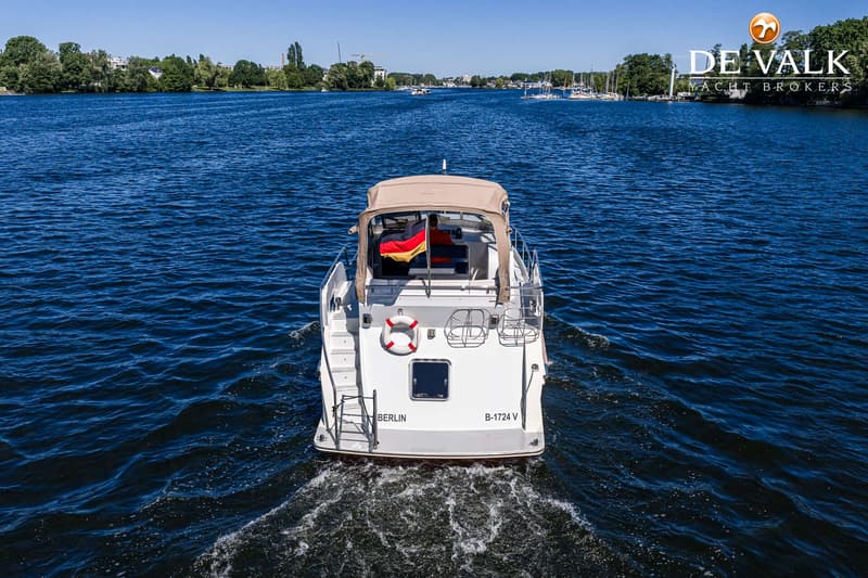 Een witte motorboot met een Duitse vlag en een beige kap vaart op een blauw water met de tekst "BERLIN B-1724 V" op de…