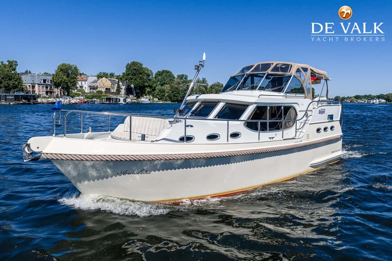 Een witte motorboot met de naam "Annabella" vaart op blauw water, met een bebouwde oever op de achtergrond.
