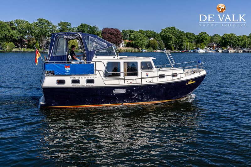 Een blauw-witte motorboot met een blauwe kap vaart op een zonnige dag over water met een persoon aan het roer.
