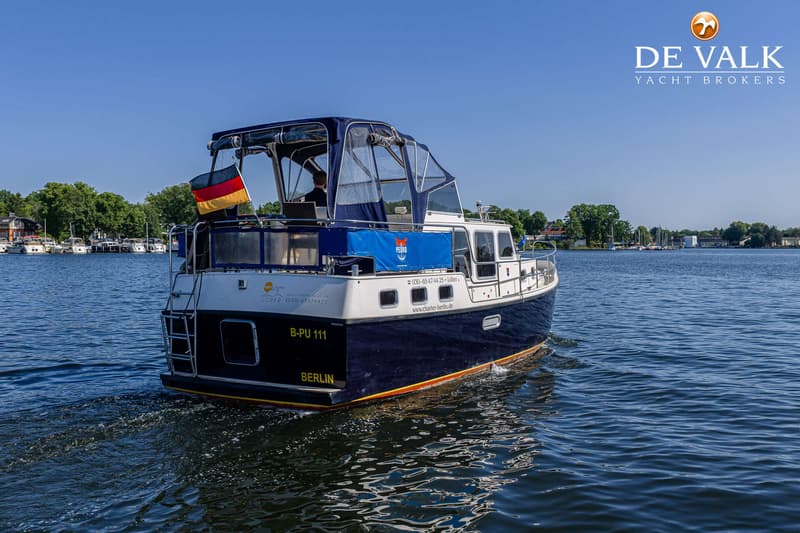Een blauw-witte motorboot met een Duitse vlag vaart op het water, met een blauwe kap en een persoon aan het roer.