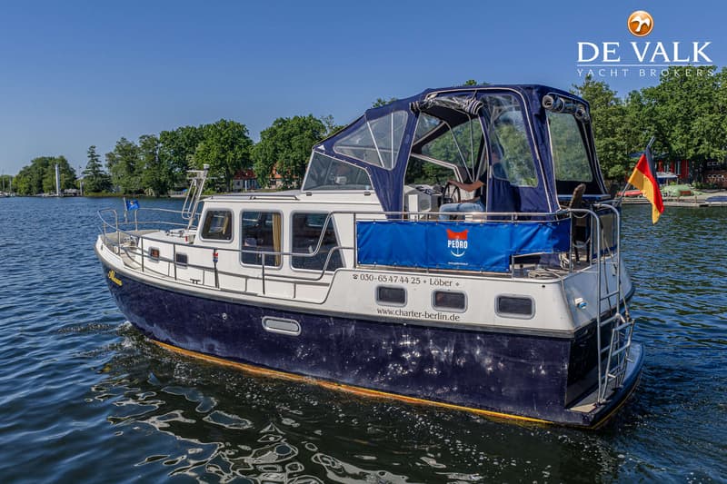 Een blauw-witte motorboot met een blauwe kap vaart op een zonnige dag over water, met bomen op de achtergrond.