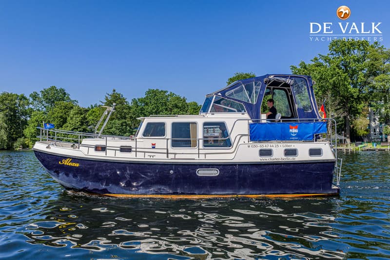 Een blauw-witte motorboot met de naam "Alexa" vaart op een waterweg met bomen op de achtergrond. — Pedro Marin 30