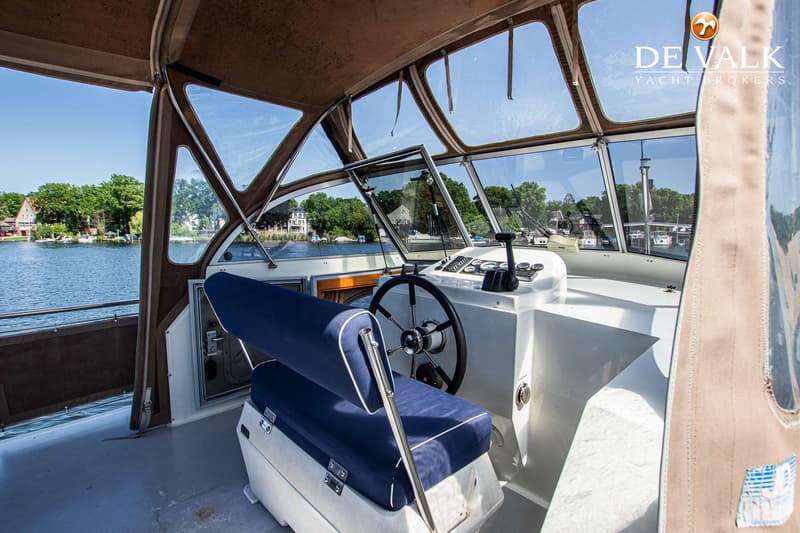 De foto toont het stuur en de blauwe zitbank van een boot, met uitzicht op water en beboste oevers. — Gruno 36 Classic