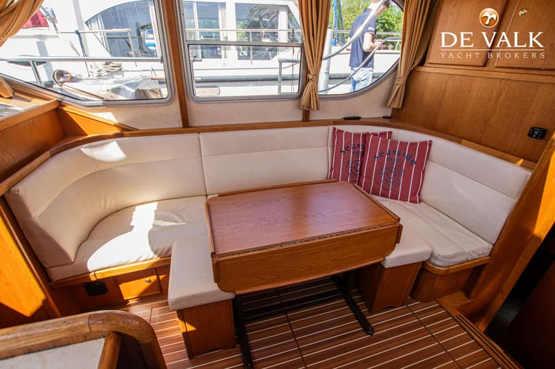 De foto toont een interieur van een boot met een U-vormige bank, een houten tafel en ramen met gordijnen. — Gruno 36 Classic