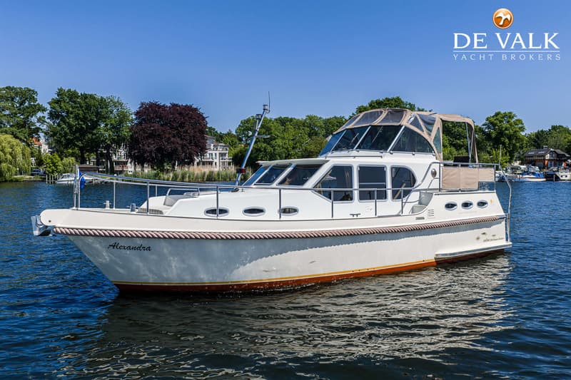 Een witte motorboot met de naam "Alexandra" vaart op een waterweg met bomen en huizen op de achtergrond. — Gruno 36 Classic