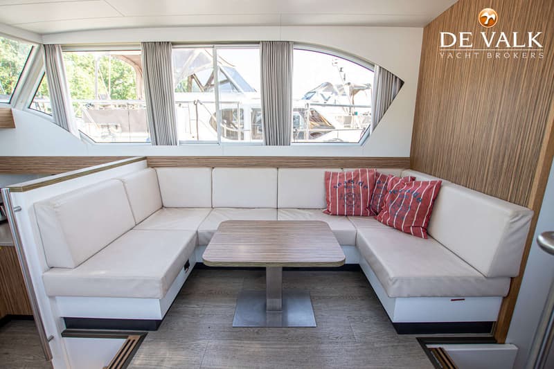 Een interieur van een boot met een U-vormige bank, een tafel en ramen met uitzicht op een andere boot. — Linskens Catfish 46