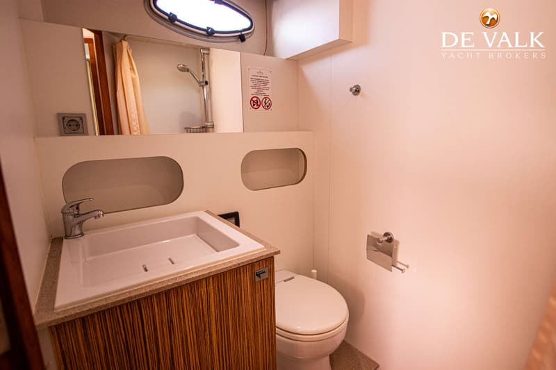 Een badkamer met een wastafel, spiegel, douchekop, toilet en een patrijspoort is zichtbaar.