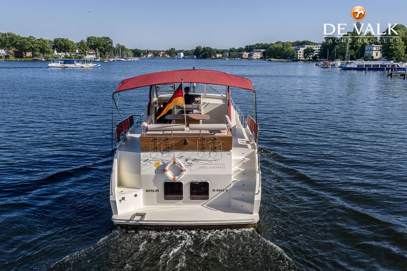 Een witte motorboot met een rood zonnedek en een Duitse vlag vaart op een meer, met een man aan het roer.