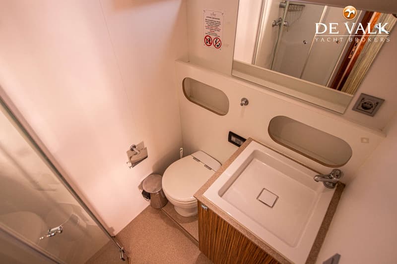 Een badkamer met een toilet, wastafel, spiegel, douchecabine en een afvalbakje.