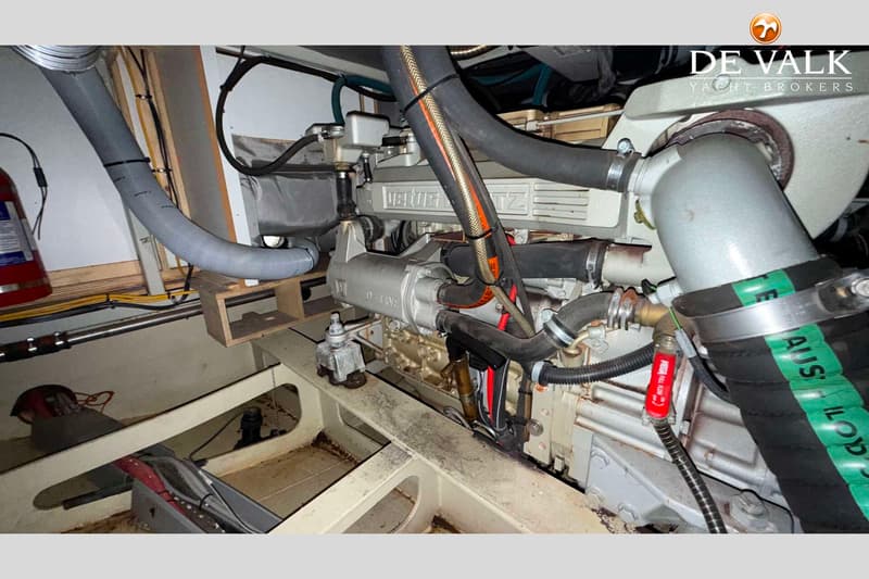 Een detailfoto van een scheepsmotor met diverse slangen, kabels en een brandblusser op de achtergrond.