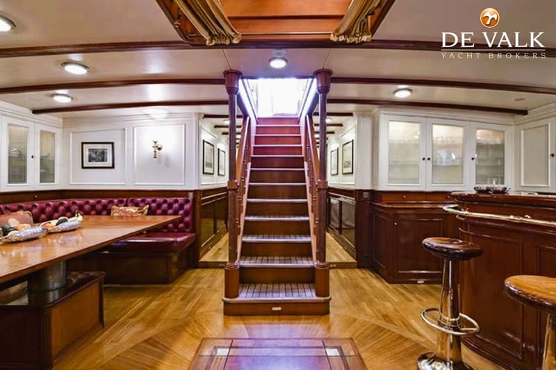 De foto toont het interieur van een boot met een houten trap, een zithoek met rode bekleding en een bar.