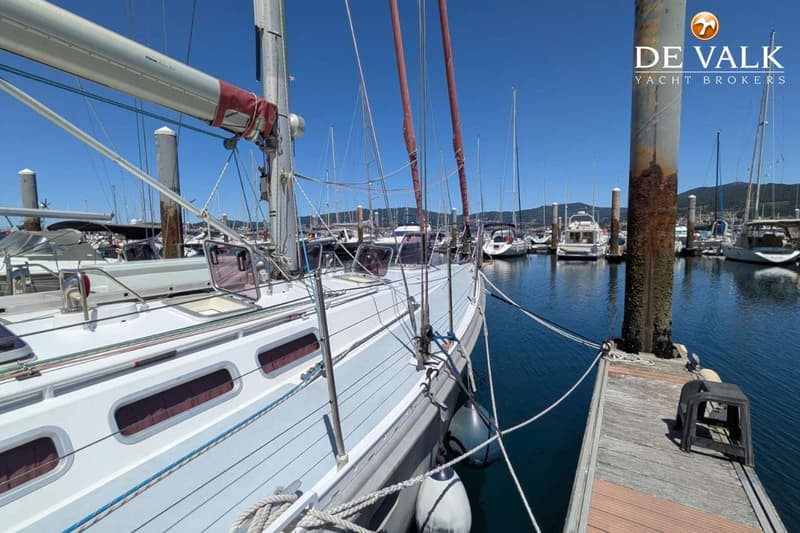 Een witte zeilboot ligt afgemeerd aan een houten steiger in een jachthaven onder een helderblauwe lucht. — Van de Stadt 48