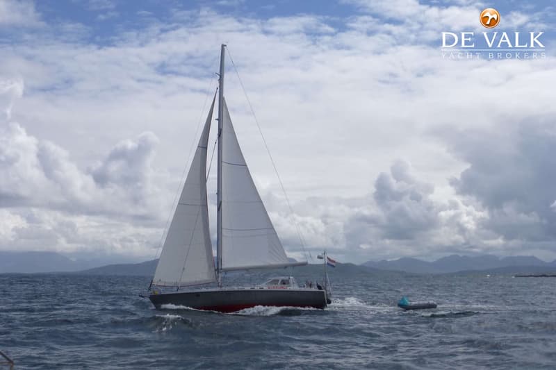 Een zeilboot met grijze romp en rode onderkant vaart op open water onder een bewolkte hemel. — Van de Stadt 48