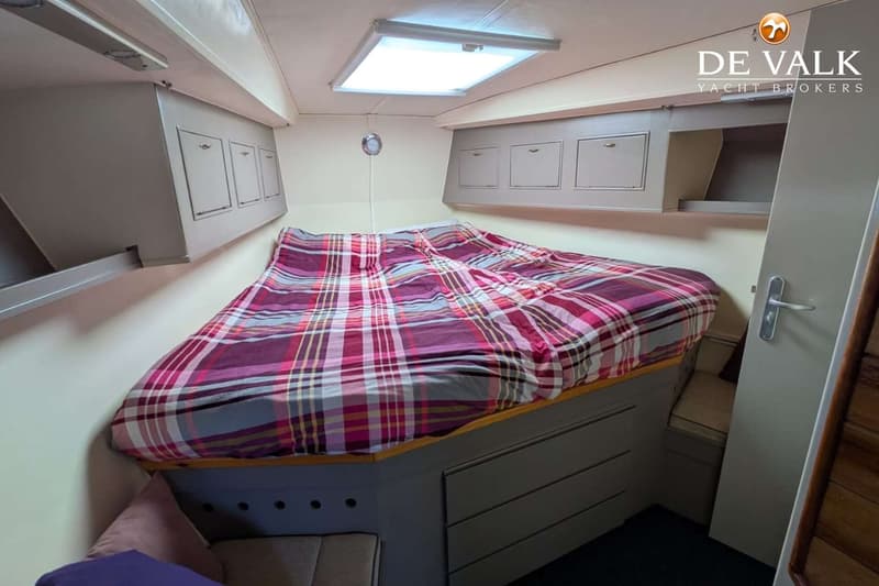 Een kajuit met een bed met geruit dekbed, opbergkasten boven het bed en een dakraam. — Van de Stadt 48