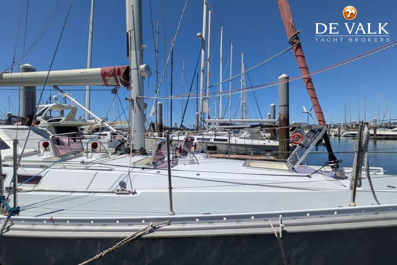 Een witte zeilboot met een grijze romp ligt afgemeerd in een haven onder een helderblauwe lucht. — Van de Stadt 48