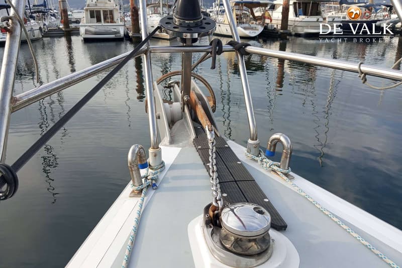 De boeg van een zeilboot met een ankerlier, ankerketting en een anker in de ankerrol, met op de achtergrond andere boten in…