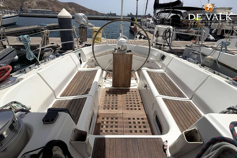 Een witte zeilboot met een houten dek en een stuurwiel, liggend in een haven. — Beneteau First 45f5