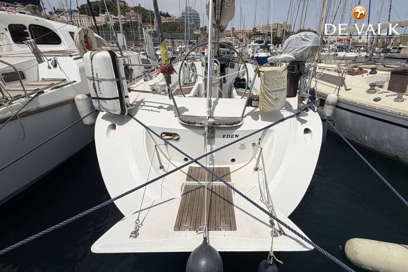 De achtersteven van een witte zeilboot met de naam "EDEN" is te zien, afgemeerd tussen andere boten in een haven.