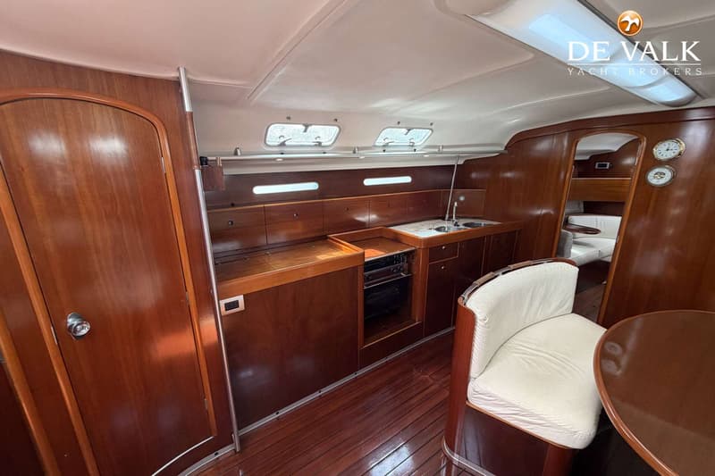 De foto toont een interieur van een boot met een kombuis, houten vloer, en een zithoek met een tafel. — Beneteau First 45f5