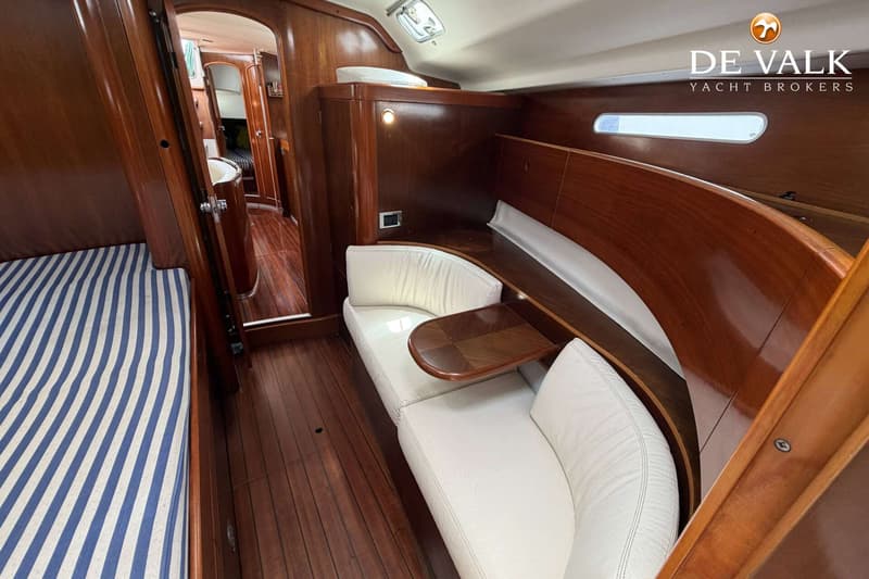 De foto toont een interieur van een boot met houten vloer en wanden, een gestreepte matras en witte banken.