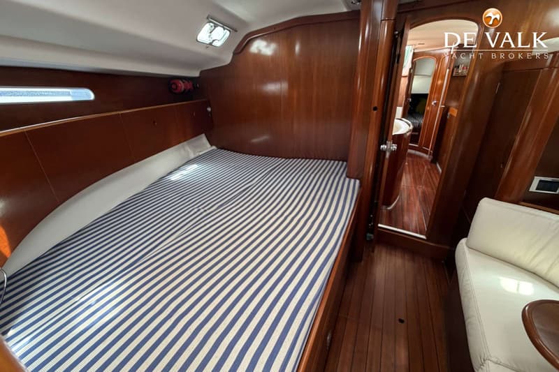 Een kajuit met een bed met blauw-wit gestreept matras, houten wanden en vloer, en een doorgang naar een andere ruimte.