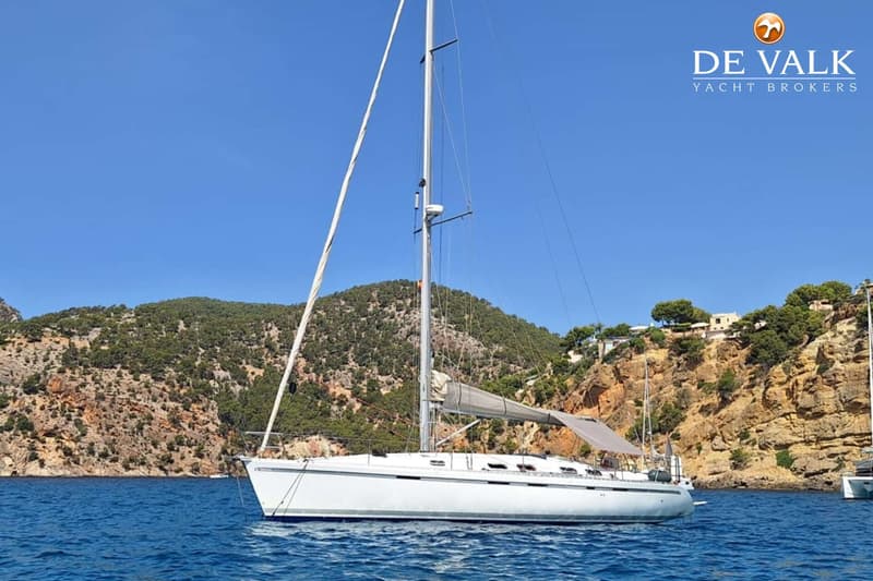 Een witte zeilboot met opgerold grootzeil en een deels opgerolde fok, ligt voor anker in een baai. — Beneteau First 45f5