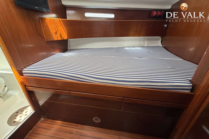 Een kajuit met een bed met blauw-wit gestreept matras, houten panelen en een kleine televisie aan de wand.