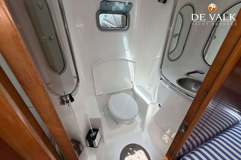 De foto toont een compacte, witte badkamer met een toilet, wastafel, spiegel en een open patrijspoort.