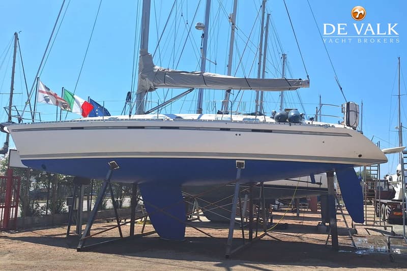 Een witte zeilboot met een blauwe onderkant staat op bokken op het droge, met vlaggen aan de reling. — Beneteau First 45f5