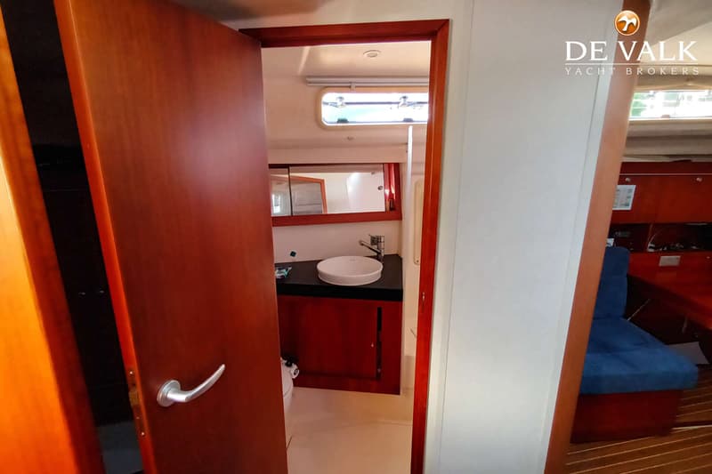 Een open deur leidt naar een badkamer met een wastafel, spiegel en een patrijspoort, met een deel van de salon zichtbaar.
