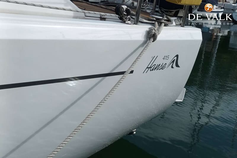 De zijkant van een witte boot met de tekst "Hanse 415" en een zwarte streep, afgemeerd in het water. — Hanse 415