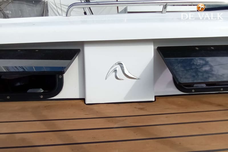 Een detail van een boot met een zilverkleurig logo op een witte romp, twee zwarte luiken en een houten dek. — Hanse 415