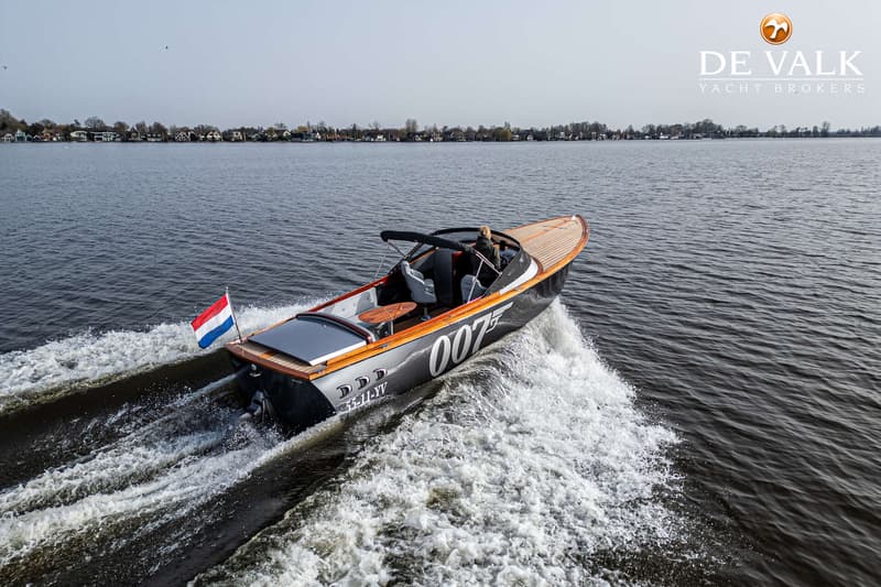 Een donkergrijze speedboot met houten dek en de cijfers "007" op de zijkant vaart over water. — Custom Aluminium Cruiser