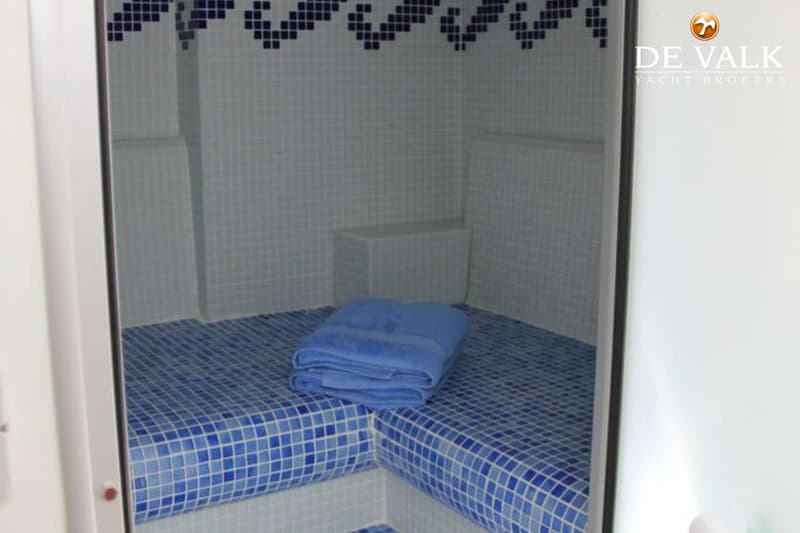 Een interieur met blauw-witte tegels, een opgevouwen blauwe handdoek op een bankje en een donkerblauw tegelpatroon bovenaan…