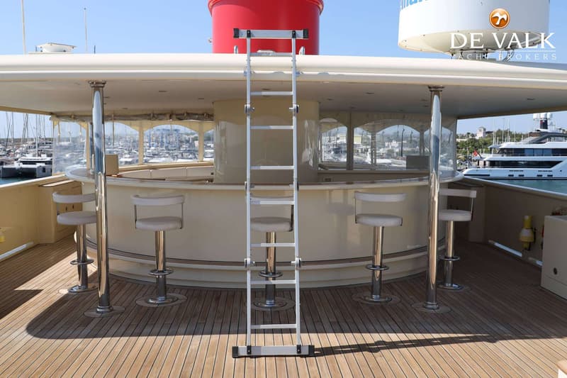 Een dek van een jacht met een bar, barkrukken, een ladder en een uitzicht op een haven. — Peer Gynt Yacht 36M Explorer
