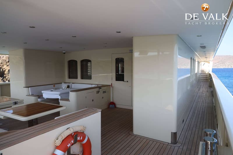 Een deels overdekt buitendek van een jacht met tafels, banken, een reddingsboei en uitzicht op zee.