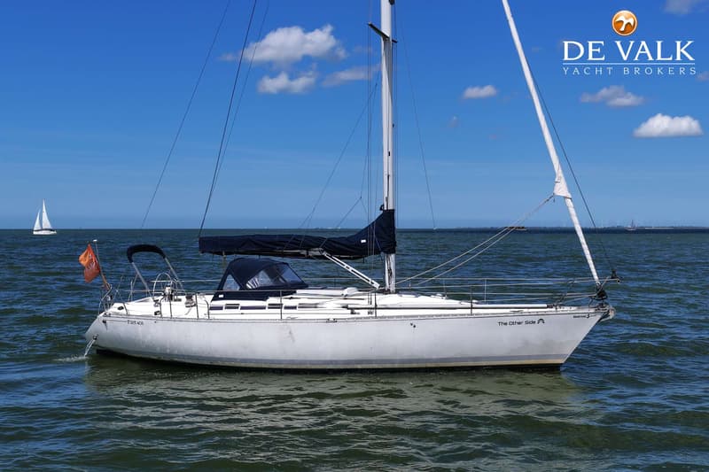 Een witte zeilboot met een zwarte huik en buiskap ligt op het water onder een blauwe lucht met wolken. — Beneteau First 405