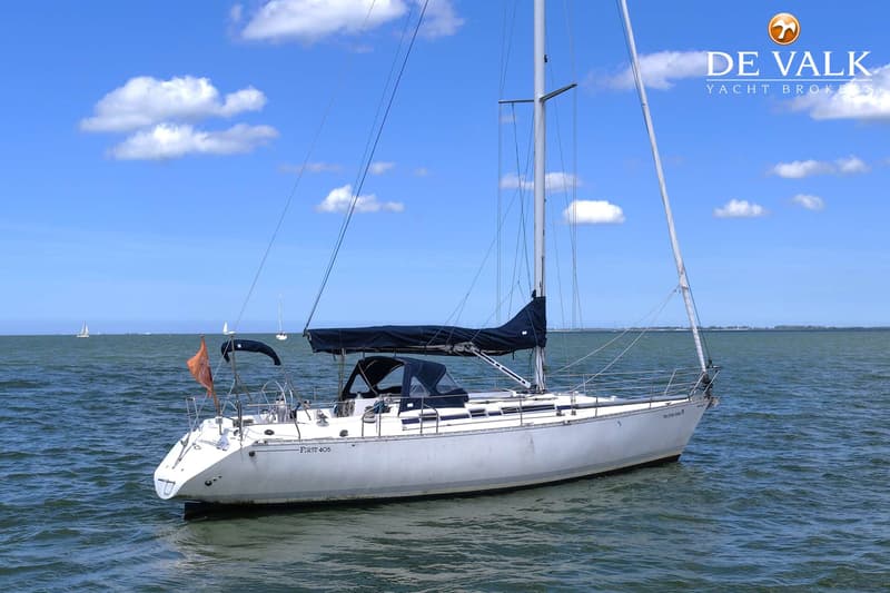 Een witte zeilboot met een donkerblauwe huik en buiskap ligt op het water onder een blauwe lucht met wolken.