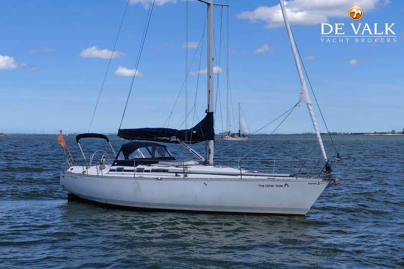 Een witte zeilboot met de naam "The Other Side" en "Beneteau" op de romp vaart op water onder een blauwe lucht.