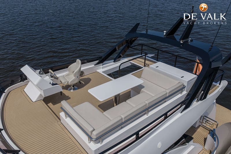 Een bovenaanzicht van het dek van een boot met een stuurstand, een witte tafel en een U-vormige bank.