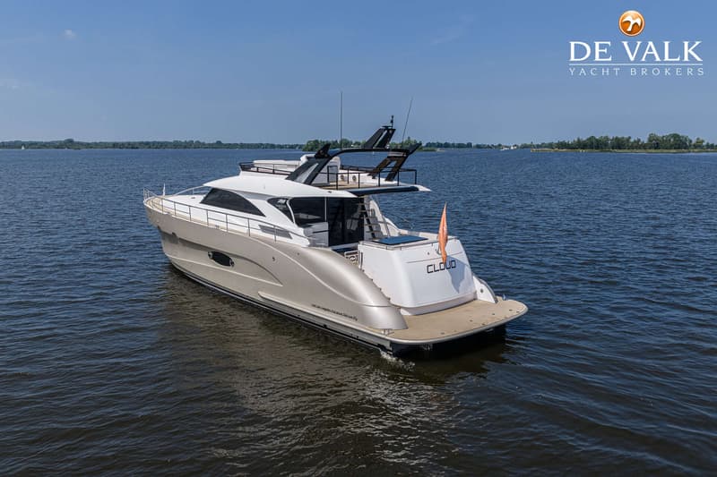 Een grote, luxe motorboot met de naam "CLOUD" op de spiegel, vaart op een meer onder een heldere blauwe hemel.