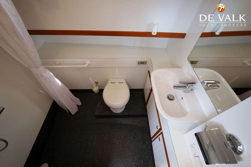 Een badkamer met een wit toilet, een witte wastafel met kraan, een spiegel, een witte douchegordijn en een donkere vloer.