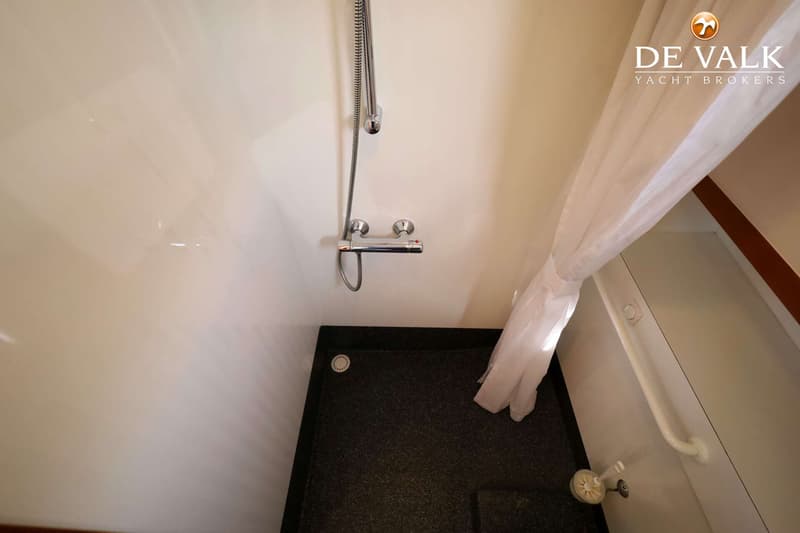 Een witte douchecabine met een zwarte antislip vloer, een douchekop, een thermostaatkraan en een wit douchegordijn.